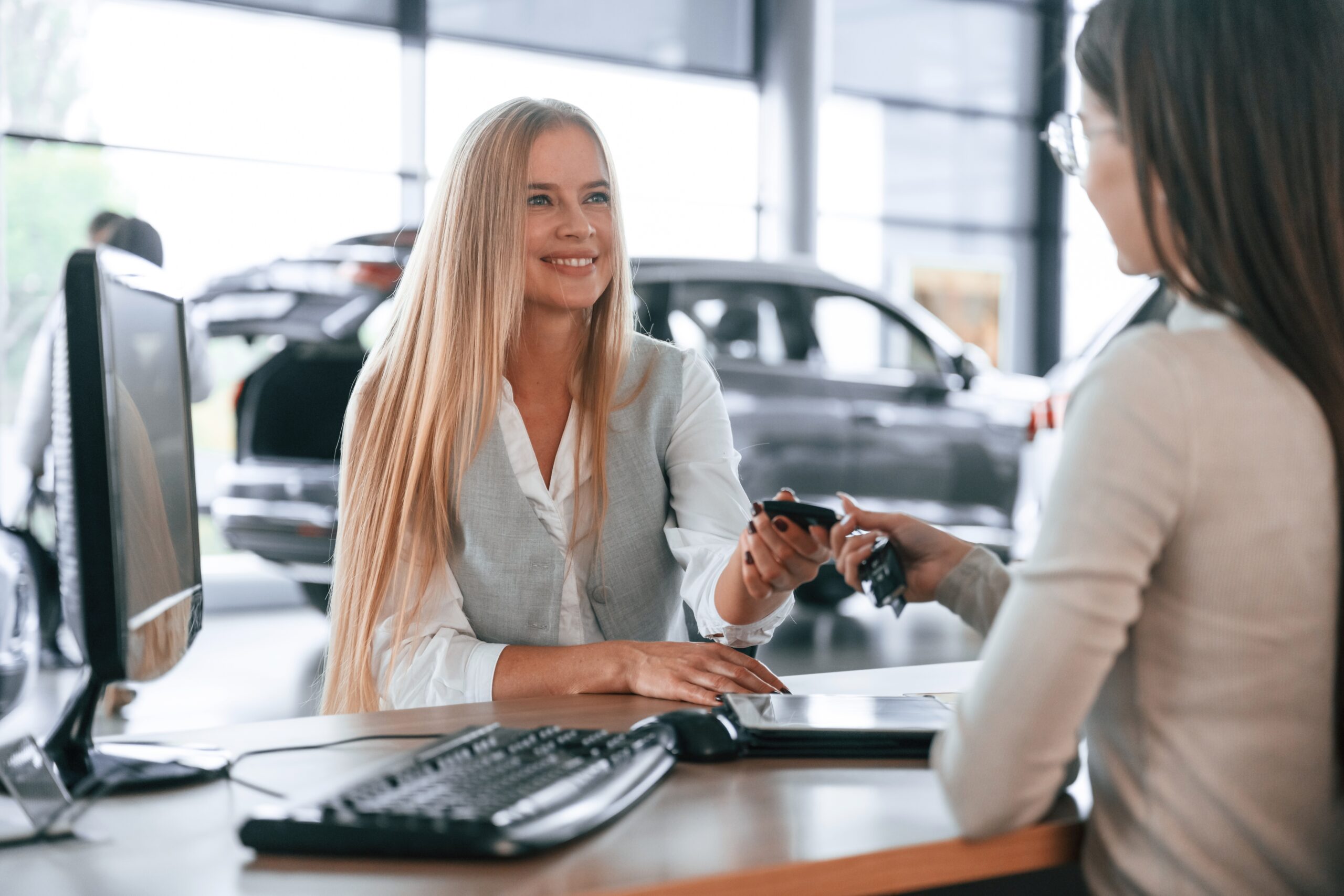 Giving the keys. Female manager is helping woman customer in the car dealership salon